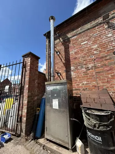 Nilfisk DTE static pressure washer fitted with a stainless steel flue extension at a brewery in Burton, installed to safely redirect boiler exhaust fumes away from a confined courtyard cleaning area.